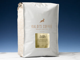 Kaldi's Colombia Community coffee bag with white packaging and a gold label against a dark blue background