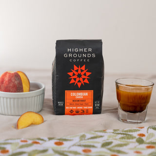 Colombian Cauca coffee bag on table with a glass of coffee and peach slices nearby