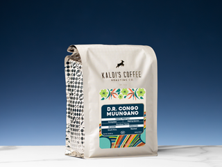 Kaldi's Coffee Muungano bag with blue label and colorful border, set on a marble surface against a deep blue sky.
