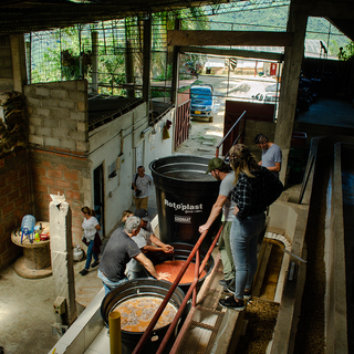 Team of workers around large fermentation tanks in a coffee processing facility.