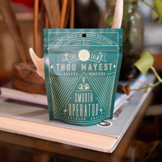 Close up of a teal Thou Mayest coffee bag on a store shelf