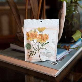 Wild Child coffee bag with yellow botanical illustration hanging in front of a chair.