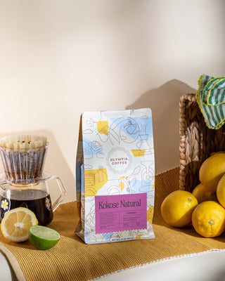 Ethiopia Kokose Natural coffee bag on a counter beside a glass coffee carafe and sliced lemons.