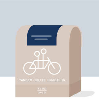 Colombia Faver Ninco Field Blend coffee bag with beige label and white bicycle graphic on a dark blue background.