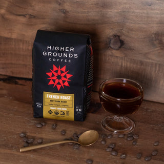 French Roast coffee bag on a wooden table with scattered coffee beans and a small glass jar nearby.