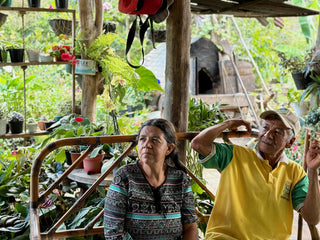 Close up of coffee beans drying on a dark mat with people visible in the background.