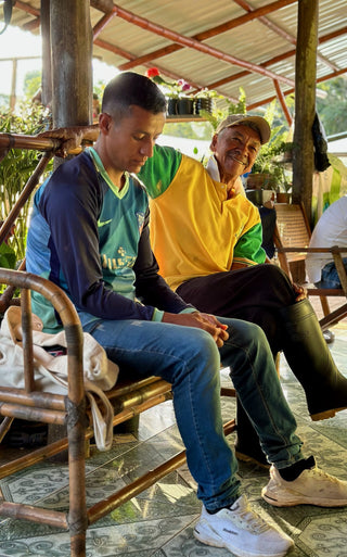 Two farmers sit on a bamboo bench under a shelter at Finca El Chaferote, sharing a moment during coffee farming.