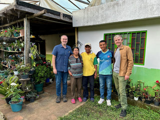 Group of five people posing outside a house with a bright green window and lush potted plants.