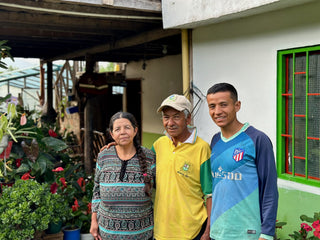 Group of people outdoors in front of a house with a bright green window and abundant potted plants.