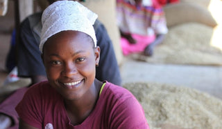 Smiling Kenyan coffee worker wearing a white headscarf at a processing site