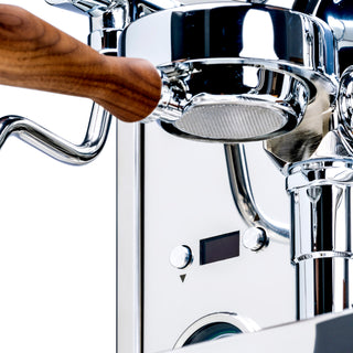 Hand inserts a stainless portafilter into a chrome LUCCA M58 Sunto espresso machine with walnut trim
