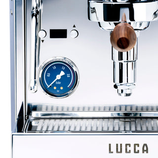 Close-up of the LUCCA M58 Sunto front panel showing a blue boiler gauge and a wooden knob on a polished chrome surface
