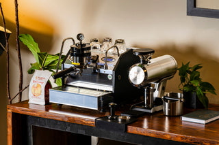 La Marzocco GS3 espresso machine with manual paddle, on a wooden counter beside a grinder and potted plants.