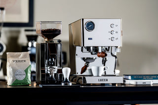 Wide side view of LUCCA Tempo espresso machine on a counter with a grinder and bag of coffee nearby