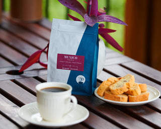 Mexico Oaxaca coffee bag on a wooden table with a cup of coffee and biscotti in the foreground