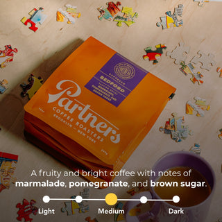Bedford espresso bag in bright orange with purple label on a puzzle piece background.