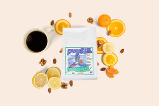 Double Double coffee bag on a beige surface surrounded by citrus slices and a cup of coffee.
