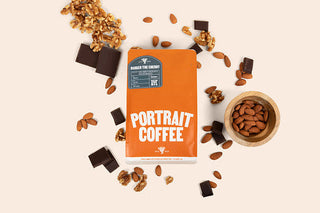Top-down shot of orange Portrait Coffee bag surrounded by almonds and chocolate pieces.