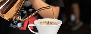 Copper kettle pours hot water into a white pour over coffee cone with a paper filter.