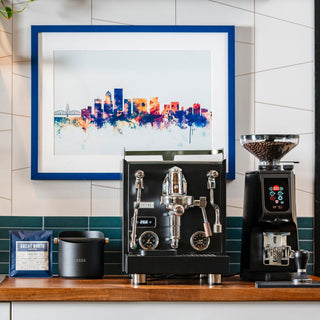 LUCCA Knock Box on a cafe counter beside an espresso machine and grinder with colorful wall art in the background