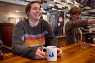 Smiling baristas at a coffee shop counter with a cup on the table, promoting Venezuela La Curva coffee.