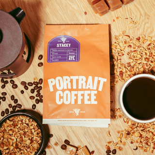 STACEY Portrait Coffee bag on a wooden table with scattered coffee beans and a cup of coffee nearby