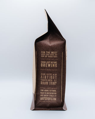 Decaf Colombia coffee bag with a folded top and brown label against a pale blue background