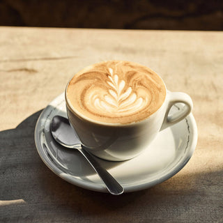 Cup of latte with rosette latte art on a white saucer and spoon on a wooden table