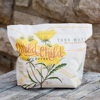 Wild Child coffee bag with bright yellow flower illustration on white packaging resting on a wooden surface.