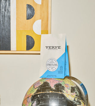 Streetlevel coffee bag by Verve with white body and blue diagonal panel beside a globe and abstract art