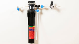 Under-sink home water filtration system with tall black filter housing and blue valve handles on white tubing.