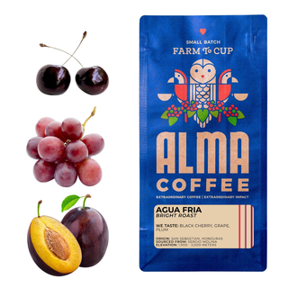 Cherries, a cluster of red grapes, and a halved plum beside a blue Alma Coffee Agua Fria bag labeled Bright Roast.