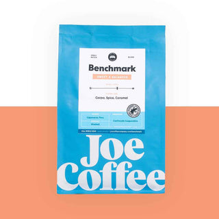 Bright blue Benchmark coffee bag with a white label and large Joe Coffee typography on a peach and white backdrop.