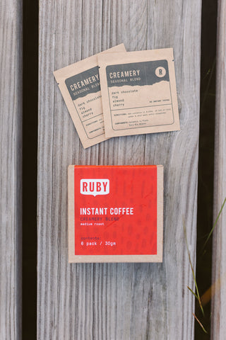 Creamery label cards on a weathered wooden surface with a Ruby Instant Coffee box nearby.