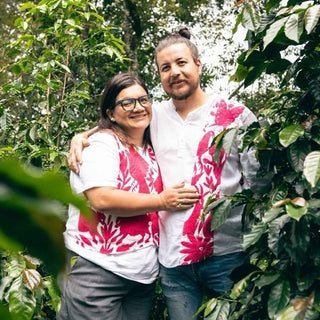 Couple embraces in a lush garden wearing white shirts with bright pink floral patterns