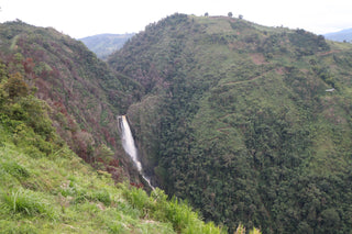 Wide view of lush Colombian hills with a tall waterfall in the valley