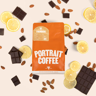 Founders coffee bag surrounded by chocolate squares almonds and lemon slices on a pale backdrop