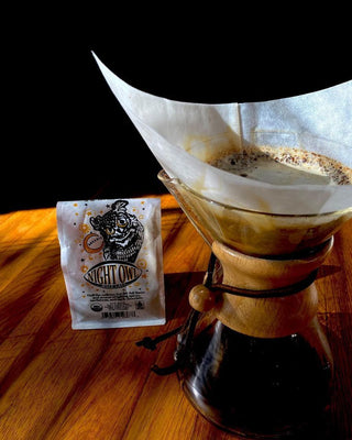 Night Owl Half-Caff coffee bag beside a glass pour over drip coffee maker on a wooden table