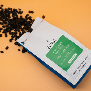 ZOKA Paladino Decaf Espresso bag with green label on orange background and scattered coffee beans.