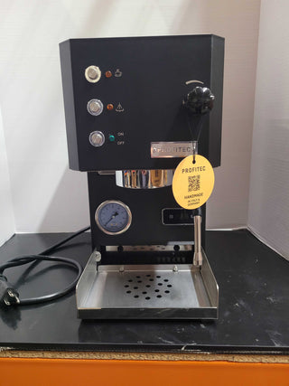 Front view of a black Profitec GO espresso machine with three chrome control dials indicator lights a portafilter on the right and a yellow tag