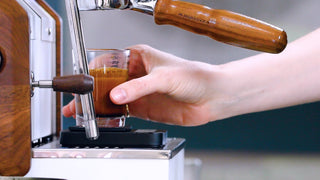 Close-up of a barista operating a commercial espresso machine with a glass under the portafilter as espresso pours.