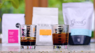 Two espresso glasses with crema on a counter with blurred packaging in the background
